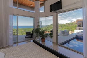A bedroom with a large window, a bed, and a view of a pool and outdoor seating area.