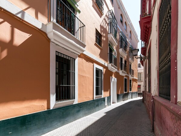A narrow cobblestone street lined with multi-story buildings featuring balconies and barred windows.