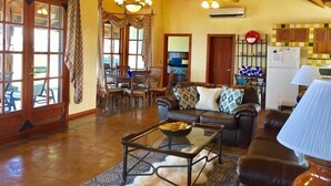 A spacious living room with a leather sofa, a glass coffee table, and a dining area with wooden chairs. - Casita Cole (Sardinal)