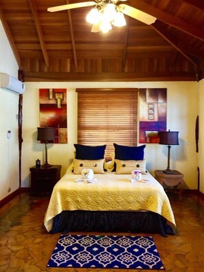 A bedroom with a bed, two nightstands, a ceiling fan, a window with blinds, and a patterned rug.