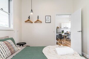 Un dormitorio con cama, mesita de noche, lámpara colgante y vista a la cocina.