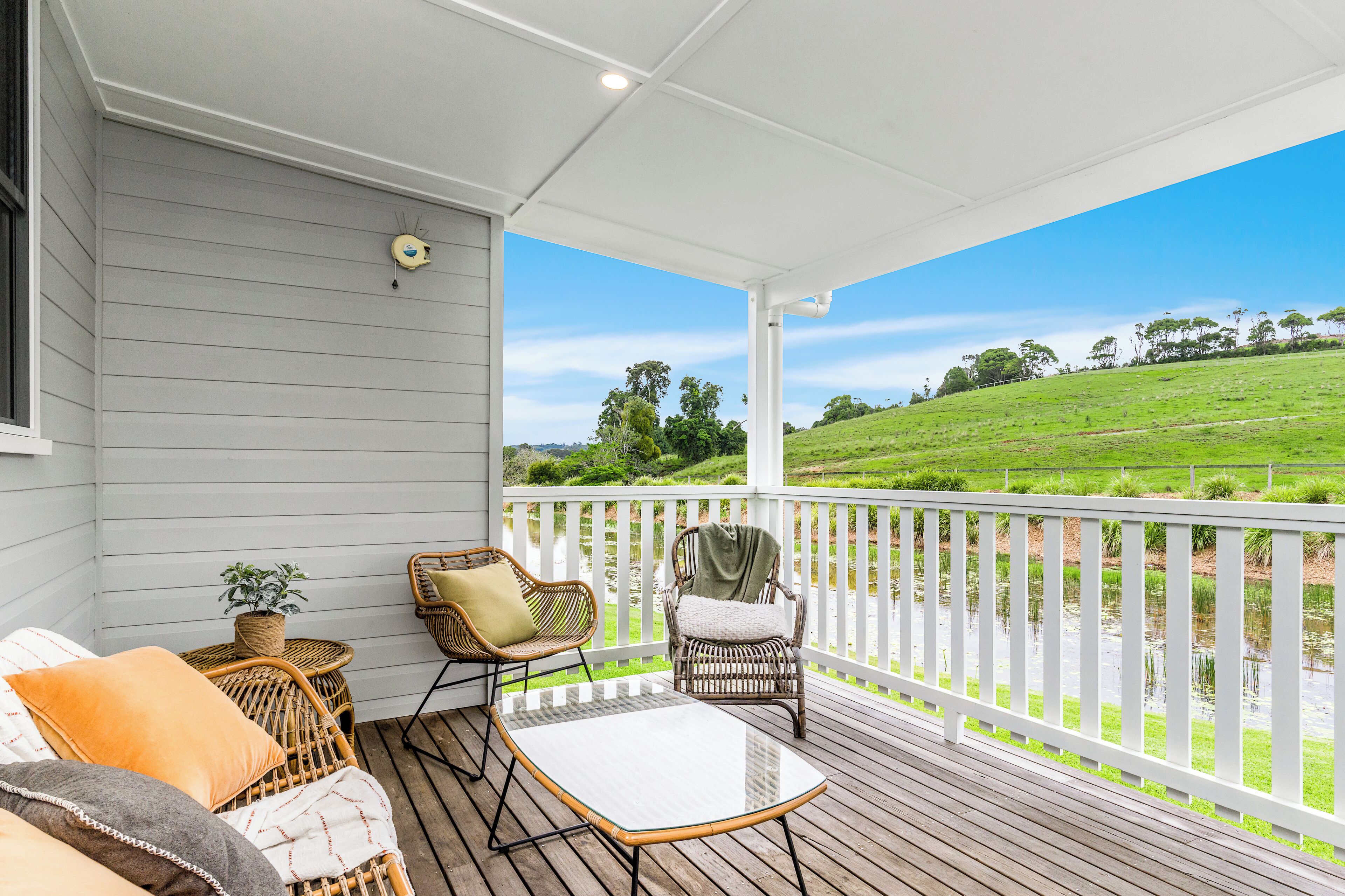 Une véranda aménagée avec des meubles en osier, une petite table et une vue sur un paysage verdoyant.