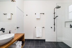 Un baño moderno con un lavamanos blanco, suelo de baldosas negras y ducha con mampara de vidrio.