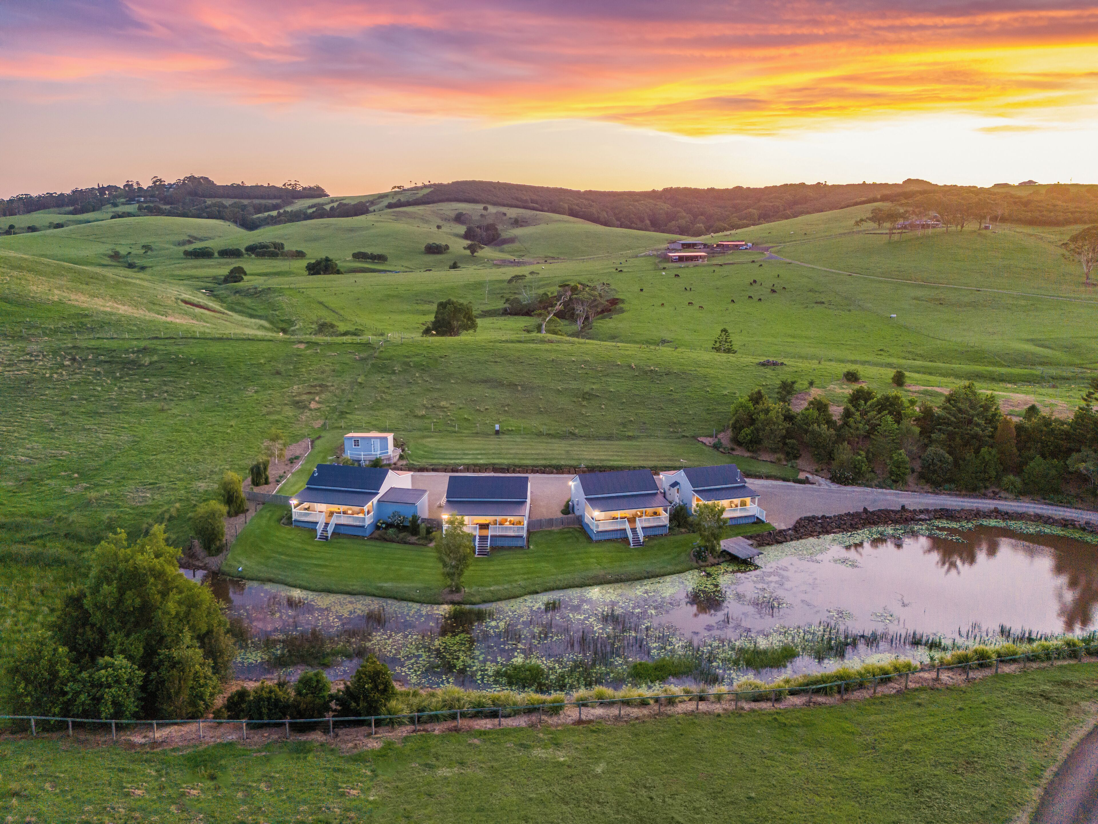 A large, open field with a small pond and a cluster of houses with a view of the surrounding landscape.