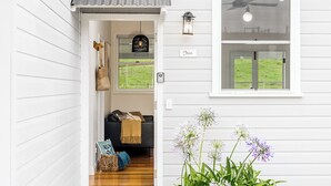 Une maison en bois blanche, avec un canapé noir, un luminaire suspendu et une fenêtre donnant sur un champ verdoyant.
