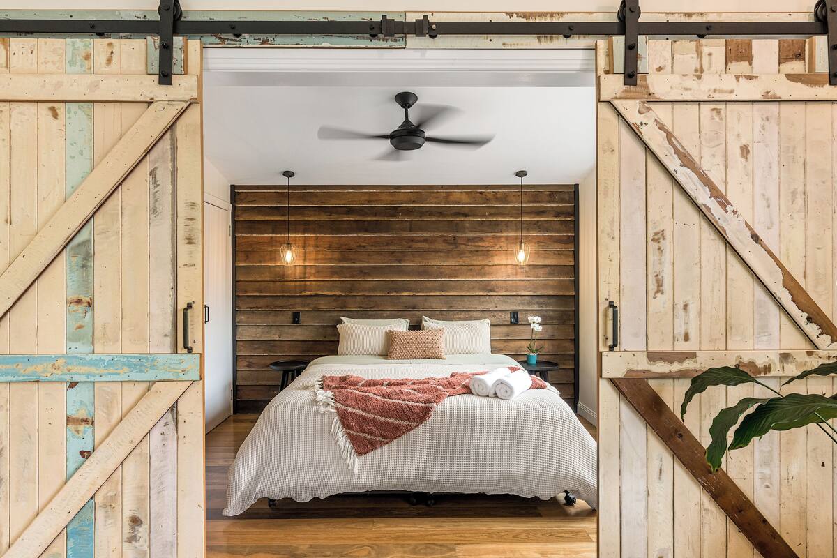 A bedroom with a wooden headboard, a ceiling fan, a bed with a striped blanket, and two pendant lights.