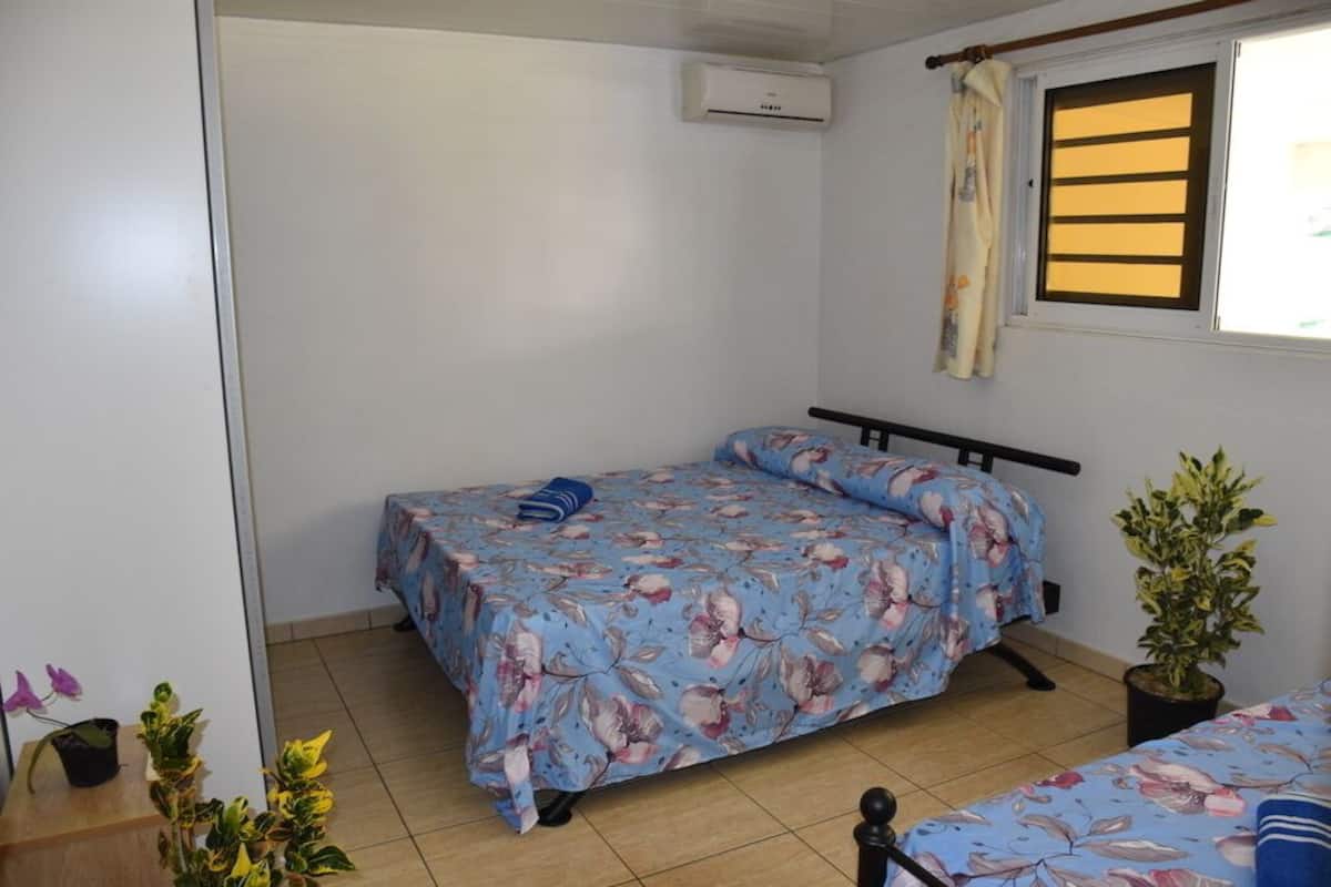 Une chambre à coucher avec un lit, une fenêtre avec des rideaux, un appareil de climatisation et une plante en pot.