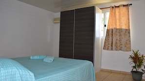 Slaapkamer met twee bedden, een garderobe, een potplant en een raam met gordijnen.