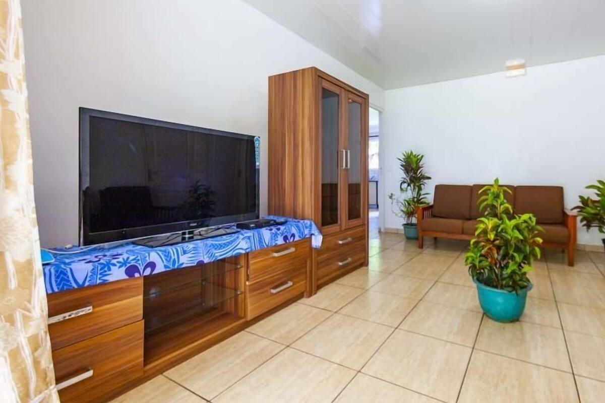 Un salon avec un téléviseur, un meuble en bois, un canapé et des plantes en pot.