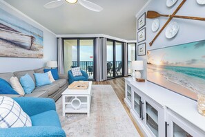 A living room with a sofa, coffee table, and artwork. There is a balcony with chairs and a view of the ocean. - Phoenix III 3035 Gulf-Front Nautical Retreat (Orange Beach)
