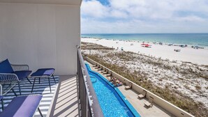 Un balcón con piscina, sillas de descanso y vista a la playa.