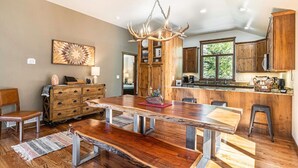 Een ruime eethoek met een grote houten tafel, een kroonluchter en uitzicht op de keuken.