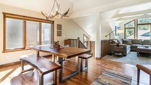 Een ruime woonkamer met een houten eettafel, een bank en een trap naar een hoger gelegen verdieping.