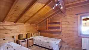 Una habitación tipo cabaña acogedora, con dos camas, paredes de madera, techo inclinado, una ventana y una pequeña mesa.