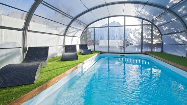 Una piscina con sillones de descanso y techo de cristal.