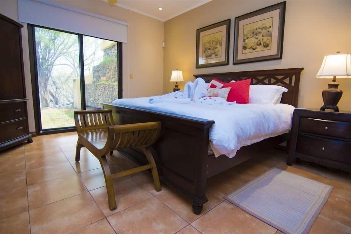 Quarto com cama, escrivaninha e cadeira. Duas luminárias de cada lado da cama.