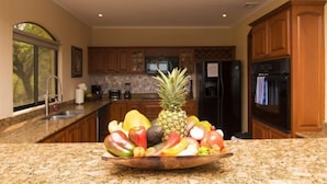 A kitchen with granite countertops, wooden cabinets, and a fruit bowl on the counter. - Mariners Point - C1 (Sardinal)