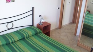 A bed with green striped bedding, a bedside table with a lamp, and a door leading to another room. - Terrazze sul Mare Alla Ciaccia - Apartment 5 (Valledoria)