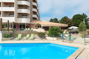 A swimming pool with lounge chairs, a covered seating area, and a building with balconies. - Super Endroit ! Appart Duplex, Accès Piscine + Spa (Saint-Jean-de-Monts)