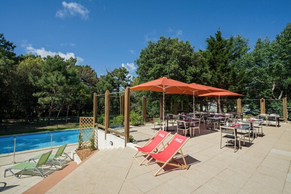 Un espace piscine extérieur doté de chaises longues et de parasols, entouré d’arbres.