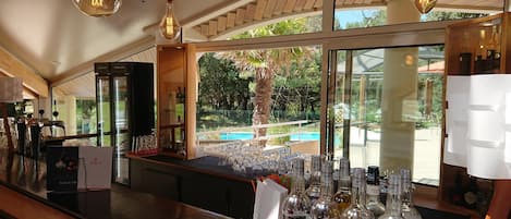 A bar area with a view of a pool and greenery outside.