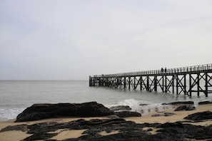 A pier extending into calm waters, surrounded by rocks and sandy beach.