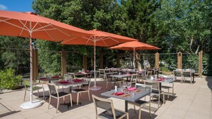 En udendørs terrasse med borde og stole, hvoraf nogle er overdækkede med parasoller.