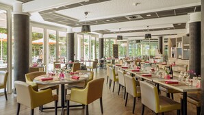 En rummelig restaurant med runde borde og gule stole, store vinduer samt et moderne loftdesign.