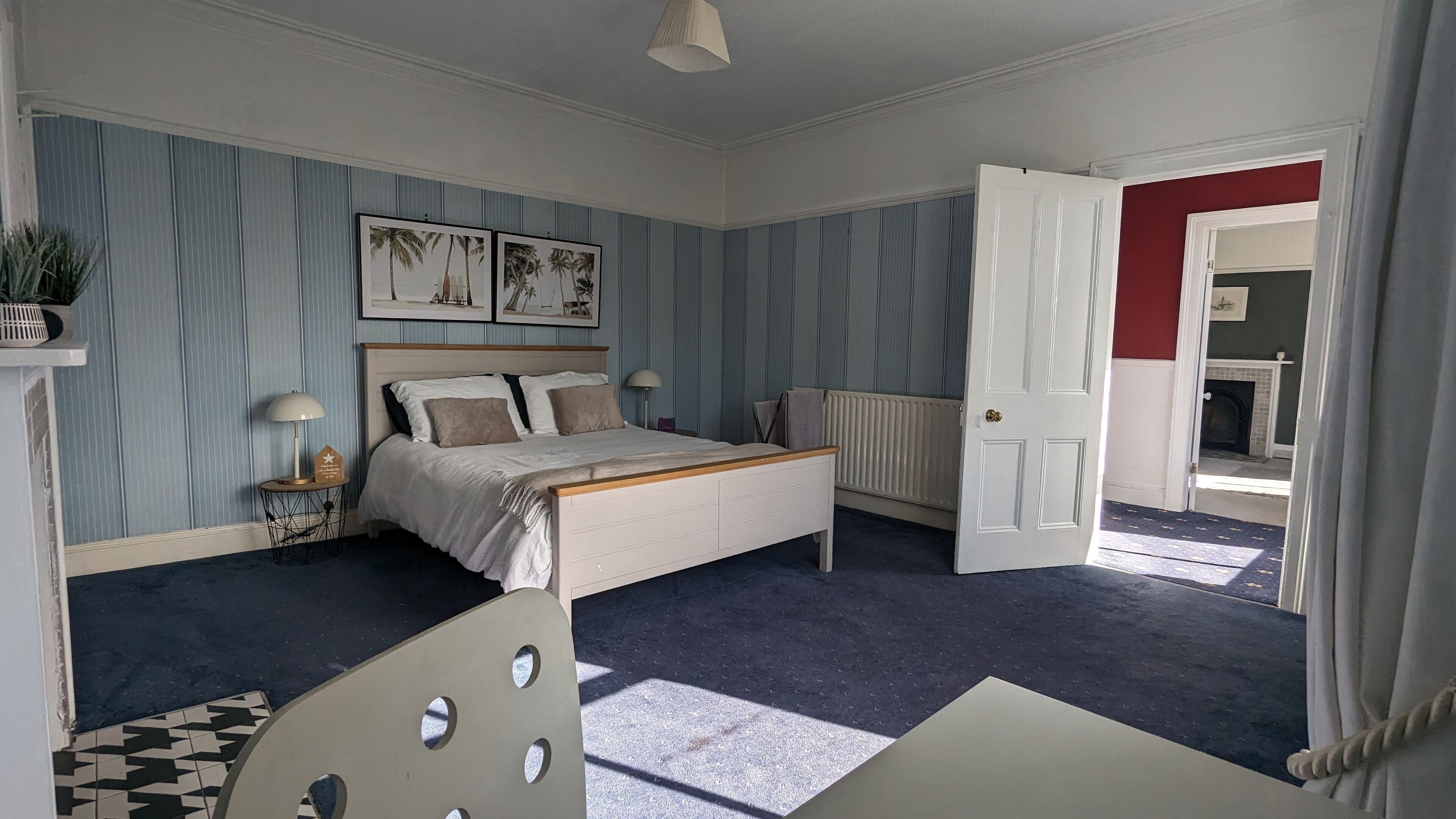 A bedroom with a bed, a radiator, a lamp, and a view of a fireplace through an open door.