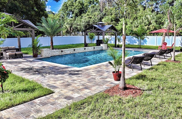 Un jardin avec une piscine, des meubles de patio et une pergola.