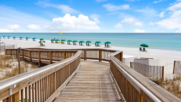 A wooden boardwalk leading to a beach with rows of green umbrellas and beach chairs. - Steps to Private Beach! Heated pool-tennis-picklebal-shuffleboard. (Destin)