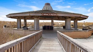 A wooden boardwalk leading to a covered pavilion with a 'Welcome To Jetty East' sign, outdoor seating, and a view of the beach. - Steps to Private Beach! Heated pool-tennis-picklebal-shuffleboard. (Destin)