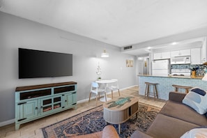 Una sala de estar moderna con un televisor de pantalla plana, un comedor con sillas blancas, una cocina con salpicadero de azulejos y una zona de estar acogedora con un tapete estampado.