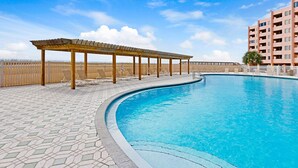 A swimming pool with a wooden pergola and lounge chairs, surrounded by a tiled deck and a fence. - Steps to Private Beach! Heated pool-tennis-picklebal-shuffleboard. (Destin)