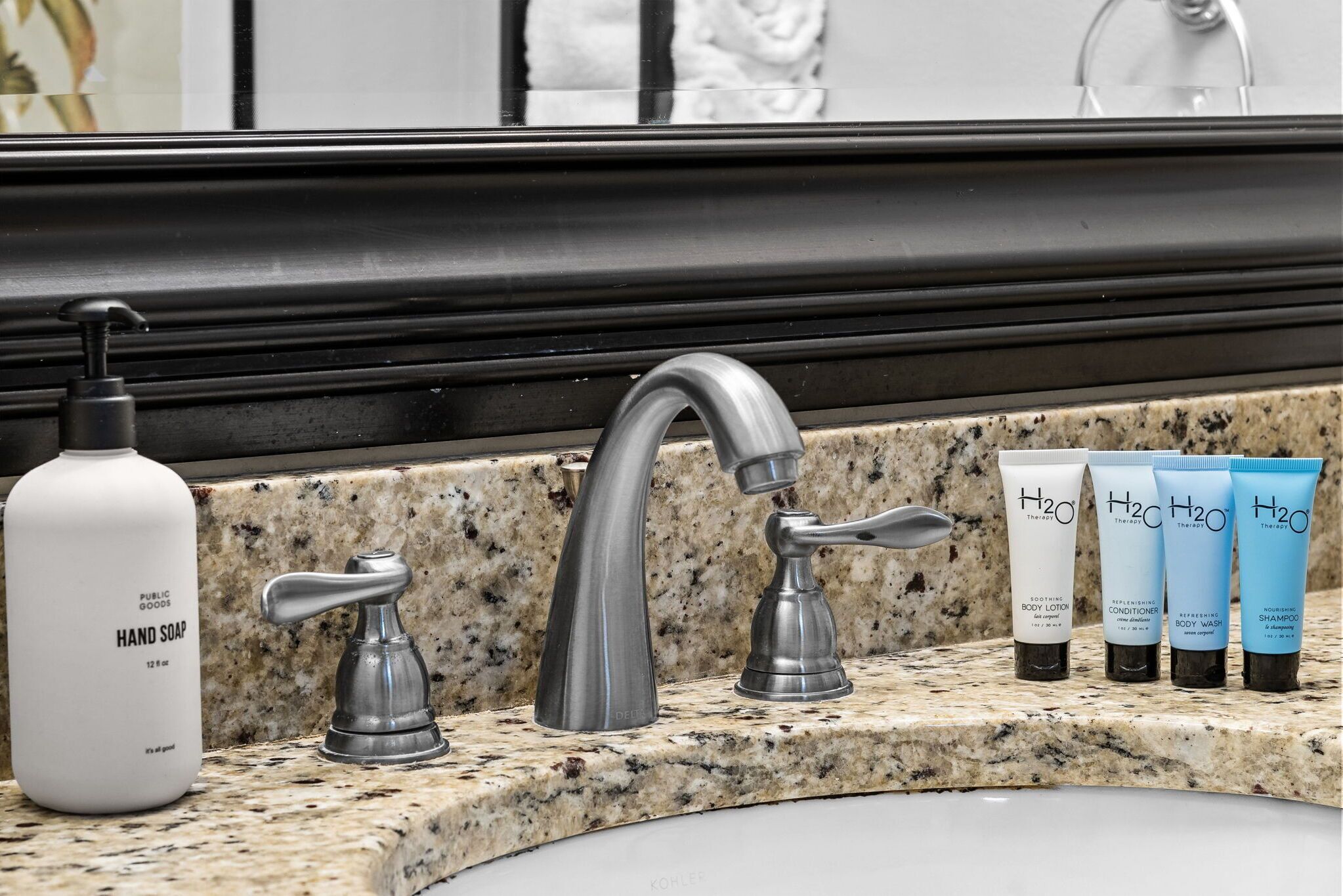 Un lavamanos de baño con un grifo moderno, una botella de jabón para manos y tres productos de cuidado de la piel H2O.