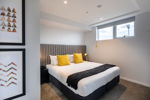 A modern bedroom with a large bed, a grey headboard, and a window with a view of a tall structure. - Linton Hotel (Kangaroo Point)