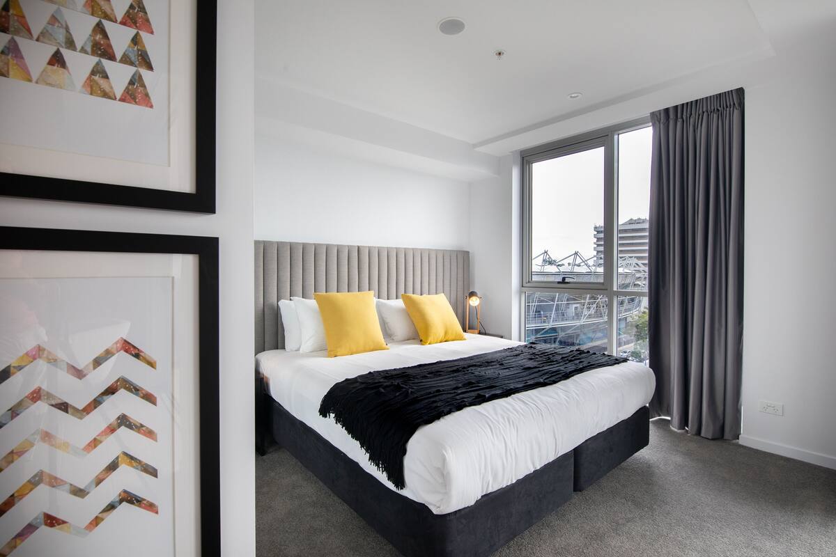 A modern hotel room with a large bed, a city view, and a framed artwork on the wall.