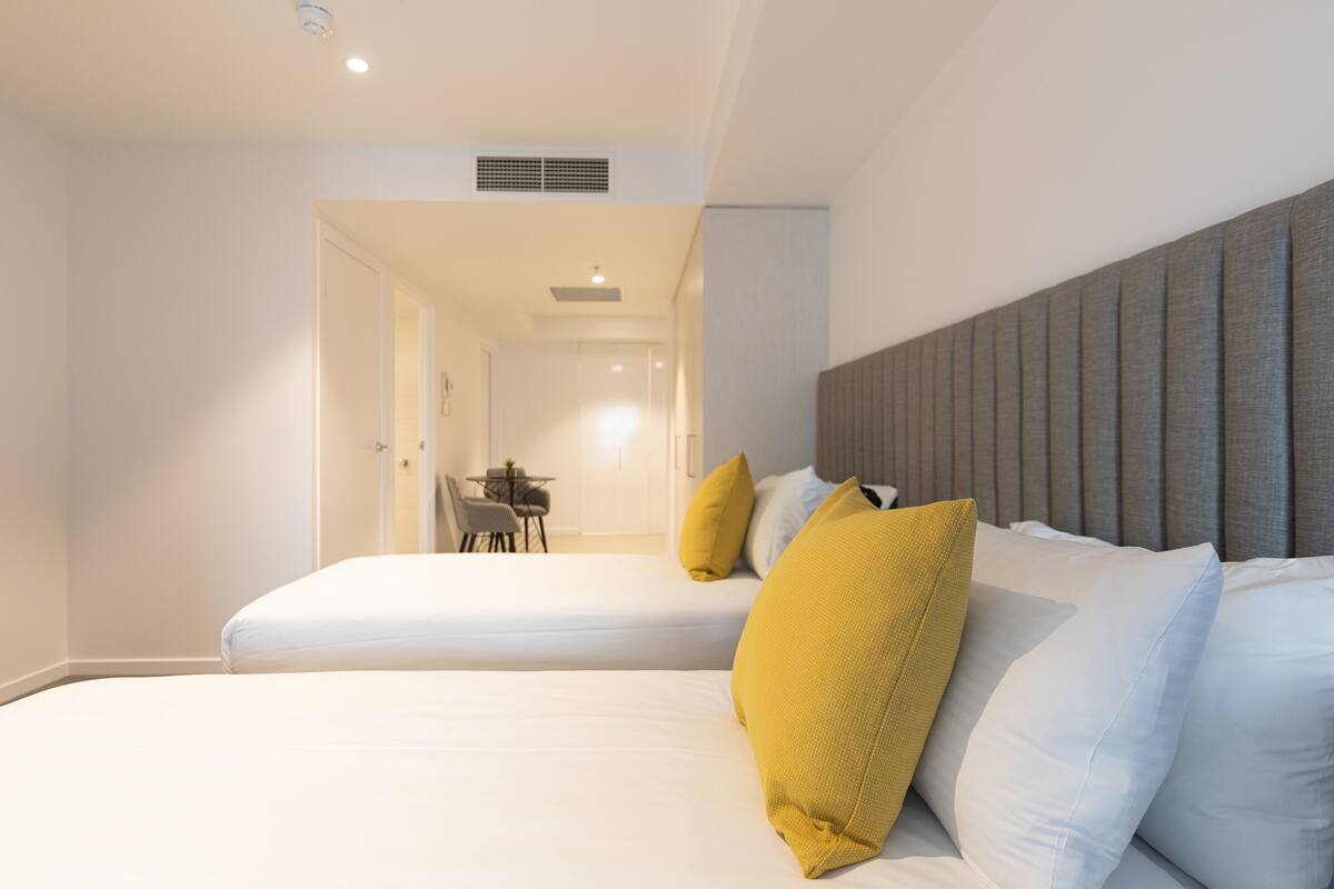 A hotel room with two beds, a dining area, and a hallway leading to another room.