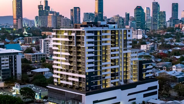 Un moderno edificio de gran altura con varios pisos y balcones, rodeado de otros edificios y zonas residenciales.
