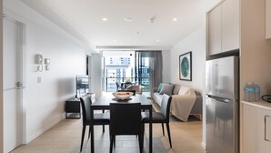 Cocina moderna con refrigerador de acero inoxidable, una mesa de comedor con sillas y vistas a la ciudad a través de amplios ventanales.