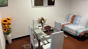 A small, modern living area with a glass dining table, white chairs, a sofa with a patterned blanket, and a vase with dried flowers. - Appartamento a Invrea Posto Auto Incluso (Genoa)