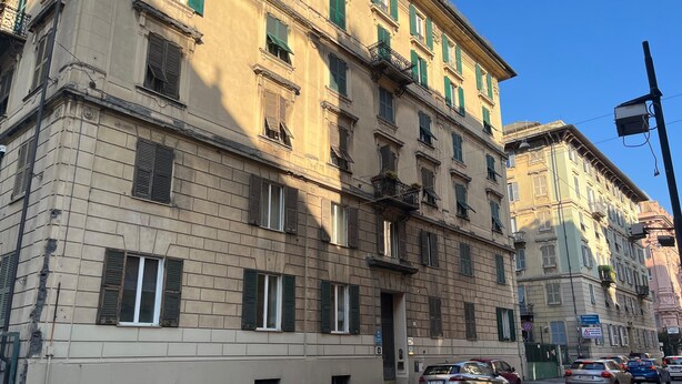 A multi-story building with a beige facade, green shutters, and a balcony with plants. - Appartamento a Invrea Posto Auto Incluso (Genoa)