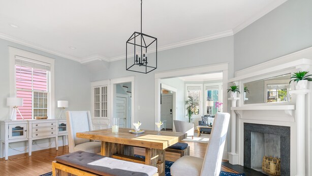 A dining area with a wooden table and benches, a fireplace, and a blue patterned rug. - Elegance Meets Ease in Historic CHS | The Rosewood (Charleston)