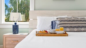 A neatly made bed with a tray of breakfast items, a bedside lamp, and a window with a view of palm trees. - Elegance Meets Ease in Historic CHS | The Rosewood (Charleston)