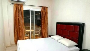 Ein Schlafzimmer mit einem Bett, einem Nachttisch, einem Sessel und einem Fenster mit Vorhängen.