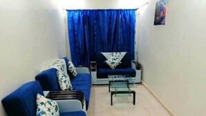 Ein Wohnzimmer mit blauem Sofa, einem Glastisch und einem blauen Vorhang.