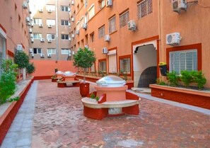 A courtyard with outdoor seating areas, a water feature, and a building with multiple windows and air conditioning units. - Perle de L'Atlas Residence 4605 (Marrakech)