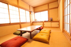 Una habitación japonesa tradicional con suelo de tatami, una mesa baja, cojines y puertas correderas.