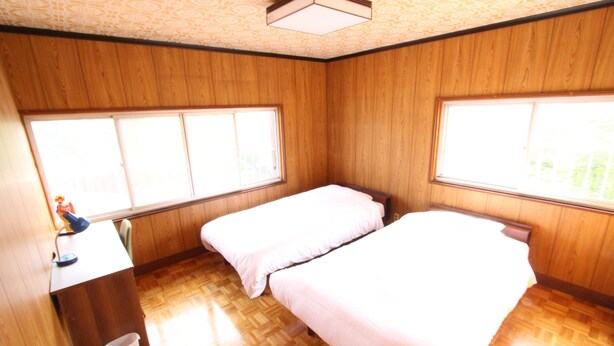 A room with wooden walls and floors, two beds, a desk with a chair, and a window. - Gran Kodachi (Fujikawaguchiko)