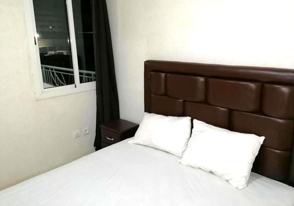 A hotel room with a single bed, a nightstand, a window with a view, and a dark brown headboard.